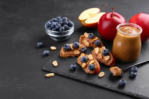 Fresh apples with peanut butter and blueberries on dark table, space for text