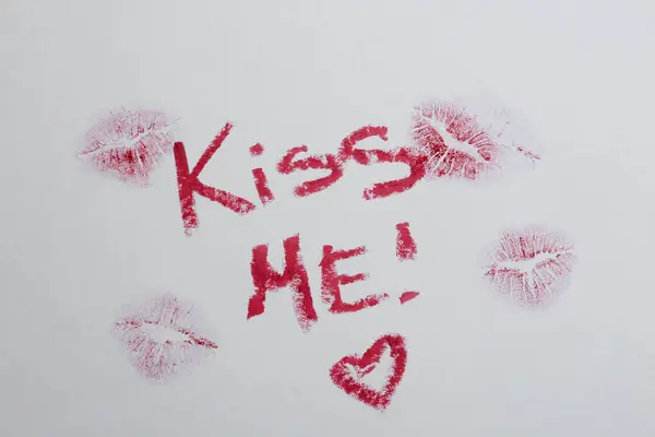 Phrase Kiss Me, marks and red heart made with lipstick on white background, above view