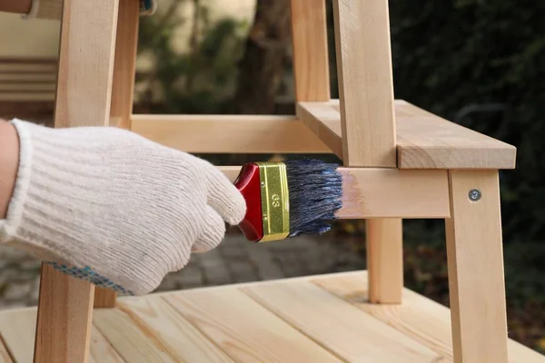Man varnishing wooden step stool at table outdoors, closeup