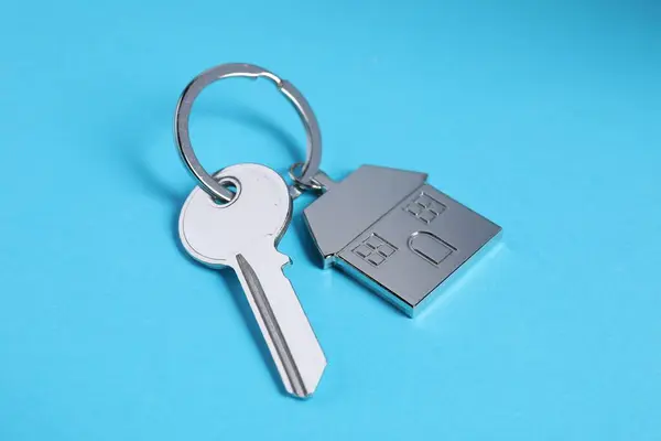Key with keychain in shape of house on light blue background, closeup