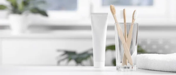 Bamboo toothbrushes in holder, toothpaste and towel on white table indoors, space for text. Banner design