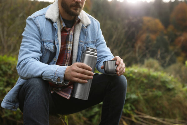 Man with metallic thermos and cup lid in nature, closeup. Space for text