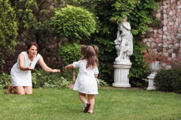 Parktaki yeşil çimlerde ilk adımı atan tatlı bir bebek. Anne ve küçük kızı birlikte vakit geçiriyorlar.