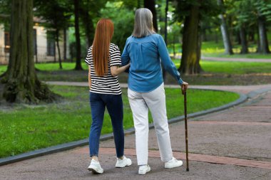 Yürüyen bastonlu yaşlı bayan ve parkta genç bir kadın.