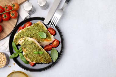 Açık gri masada servis edilen pesto soslu, domatesli ve çatal bıçaklı leziz tavuk göğsü. Metin için boşluk