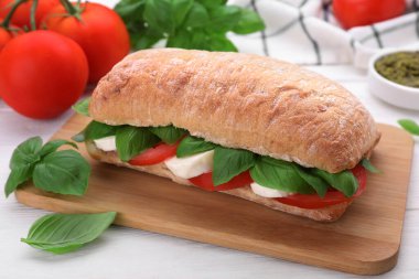 Beyaz ahşap masada mozzarella, domates ve fesleğenli lezzetli Caprese sandviçi, yakın plan.