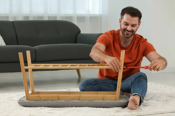 Man assembling shoe storage bench with screwdriver on floor at home