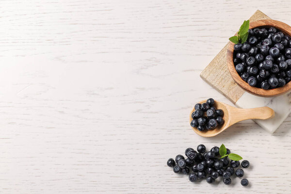 Ripe bilberries and leaves on white wooden table, flat lay. Space for text