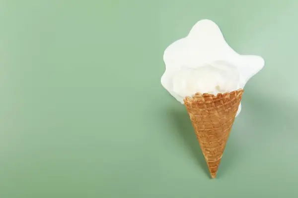 Melted ice cream and wafer cone on green background, top view. Space for text