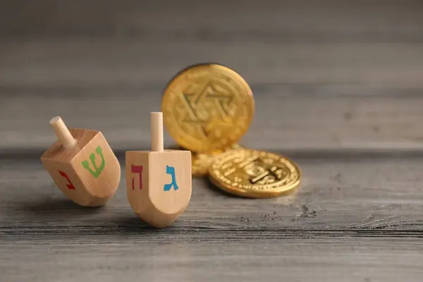 stock image Dreidels with Jewish letters and coins on wooden table, space for text. Traditional Hanukkah game