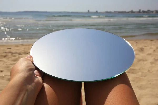 Woman with round mirror reflecting sky on beach, closeup