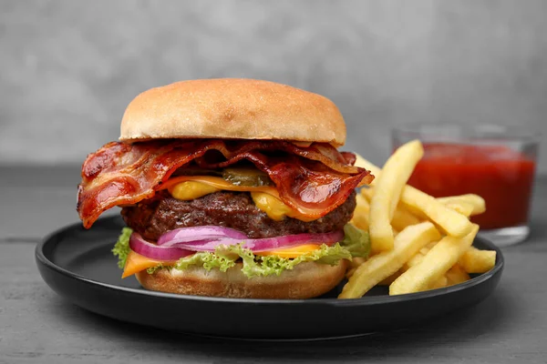 Tasty burger with bacon, vegetables and patty served with french fries on grey wooden table, closeup