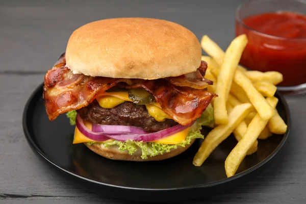 Tasty burger with bacon, vegetables and patty served with french fries and ketchup on grey wooden table, closeup