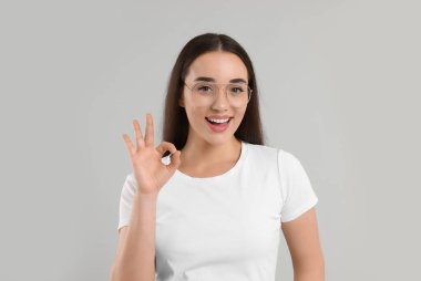 Gözlüklü güzel bir kadın açık gri arka planda güzel bir jest yapıyor.