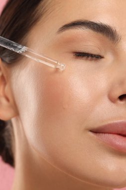 Güzel genç bir kadın yüzüne serum sürüyor, yakın plan.