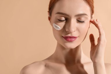 Yüzünde bej arka planda güneş kremi olan güzel genç bir kadın. Mesaj için yer var.