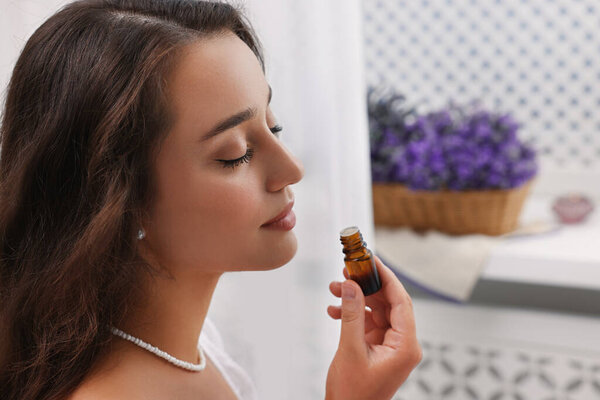 Beautiful young woman with bottle of essential oil indoors