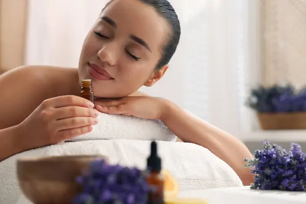 Beautiful young woman with bottle of essential oil on massage couch in spa salon