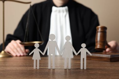 Family law. Judge with gavel and scales of justice sitting at wooden table, focus on figure of parents and children clipart