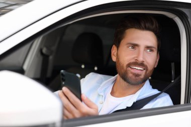 Arabadaki akıllı telefonu kullanan mutlu sakallı adam, dışarıdan görüyor.