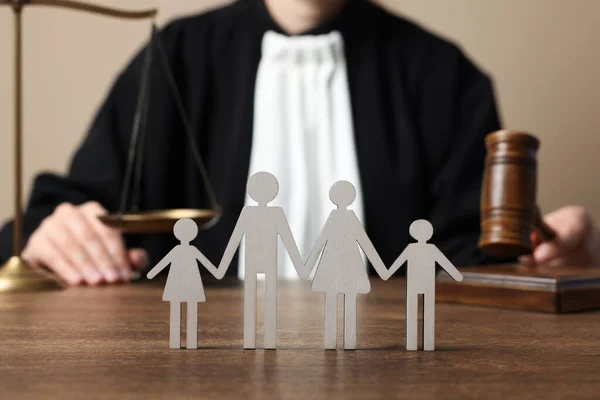 Family law. Judge with gavel and scales of justice sitting at wooden table, focus on figure of parents and children