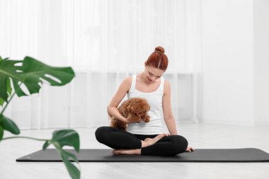 Kapalı alanda sevimli köpeğiyle yoga yapan genç bir kadın.