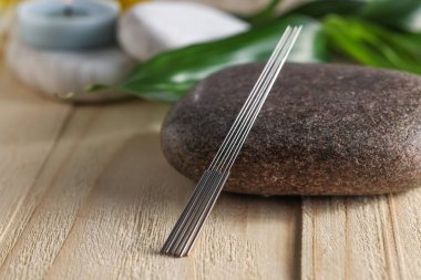 Akupunktur iğneleri ve spa taşı ahşap masada, yakın plan.