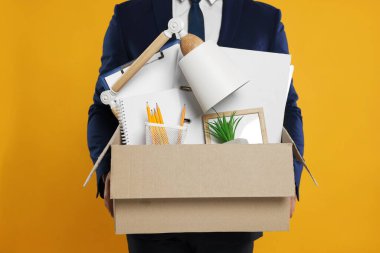 Turuncu arka planda kişisel ofis eşyaları olan işsiz bir adam, yakın plan.