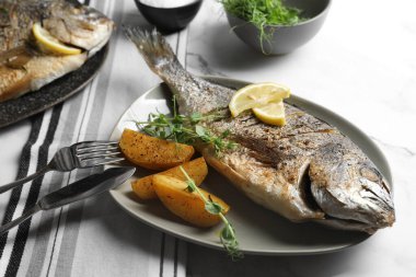 Deniz ürünleri. Limon, patates ve mikroyeşilliklerle servis edilen enfes fırınlanmış balıklar, yakın plan.