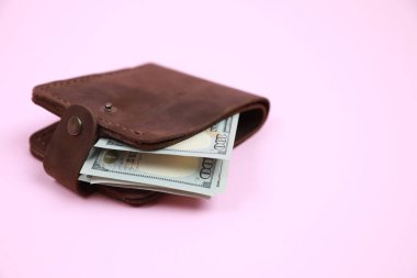 Pembe arka planda dolar banknotları olan şık kahverengi deri cüzdan, yakın plan. Metin için boşluk