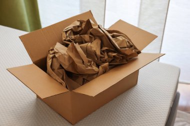 Beyaz şiltenin içinde buruşmuş kahverengi kağıt dolgu malzemesi olan karton kutuyu aç.