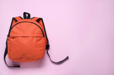 Mor arka planda turuncu bir sırt çantası, üst manzara. Metin için boşluk
