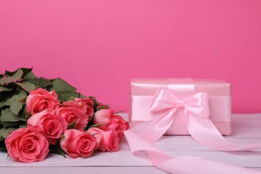 Beyaz ahşap masada pembe arka planda güzel güller ve yaylı hediye kutusu, metin için boşluk