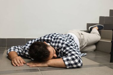 Bilinçsiz bir adam merdivenlerden düştükten sonra yerde yatıyor.