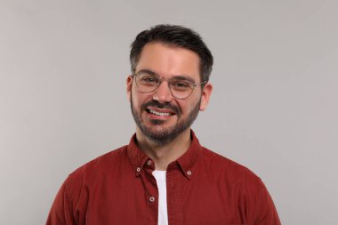 Açık gri arka planda şık gözlüklü mutlu bir adamın portresi.