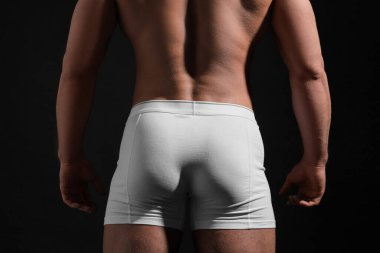 Siyah arka planda beyaz iç çamaşırlı genç adam, yakın plan.