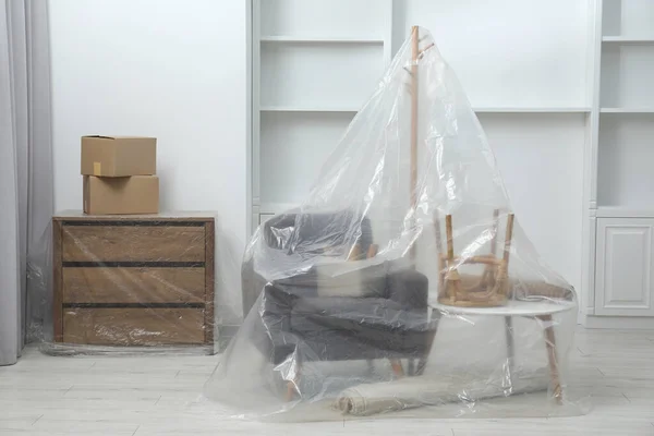 Modern furniture covered with plastic film and boxes at home