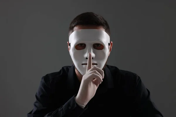 Man in mask and gloves showing hush gesture against grey background