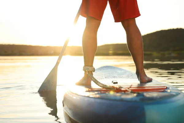 Man paddle boarding on SUP board in river at sunset, closeup