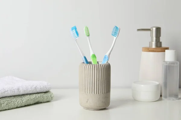 Plastic toothbrushes in holder, towels and cosmetic products on white countertop