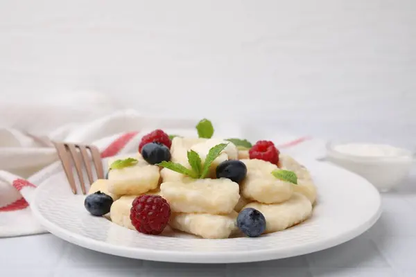 Plate of tasty lazy dumplings with berries, butter and mint leaves on white tiled table