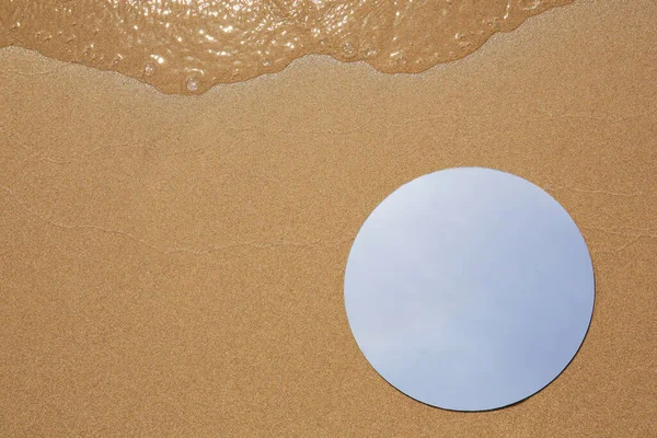 Round mirror reflecting sky on beach sand, top view. Space for text