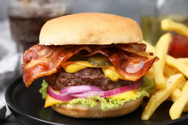Tasty burger with bacon, vegetables and patty served with french fries on table, closeup