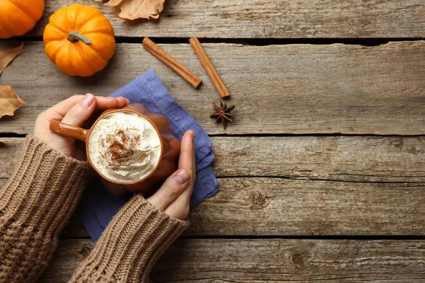 Ahşap masada elinde kremalı balkabağı aromalı latte tutan bir kadın. Metin için boşluk