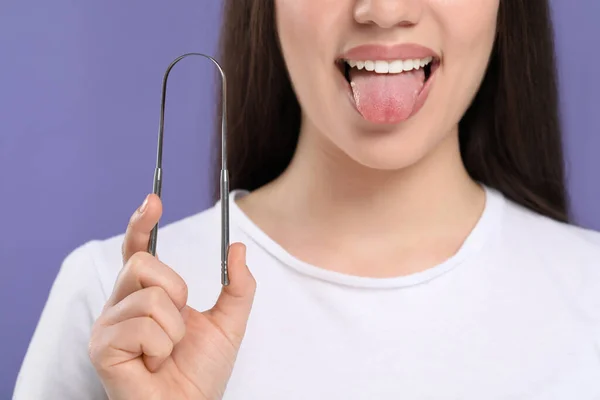 Woman with tongue cleaner on violet background, closeup