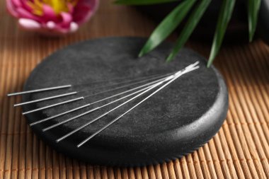 Bambu hasırının üzerinde akupunktur iğneleri ve spa taşı, yakın plan.