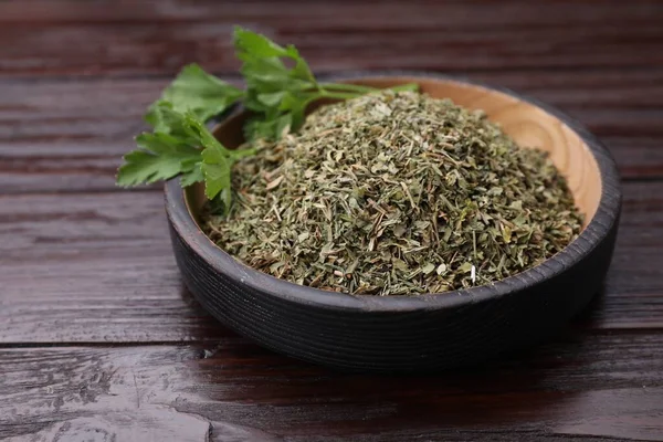 Dried aromatic parsley and fresh leaves in plate on wooden table, closeup