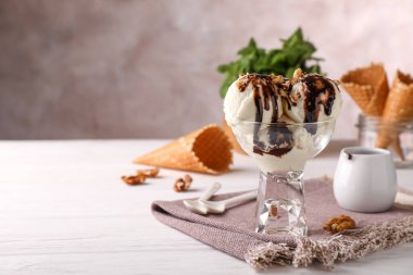 Beyaz ahşap masada servis edilen çikolata soslu ve fındıklı bir tatlı kasesi dolusu lezzetli dondurma. Metin için boşluk