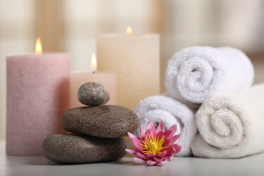 Spa kompozisyonu. Yanan mumlar, nilüfer çiçeği, beyaz masada taşlar ve havlular.
