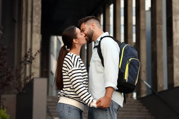 Long-distance relationship. Man with backpack kissing his girlfriend outdoors, low angle view